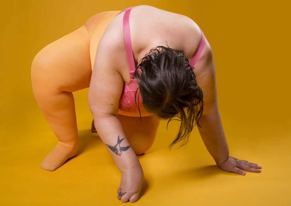 Giant dyke on the floor, pink bra, tattoos, yellow tights, power knuckle.